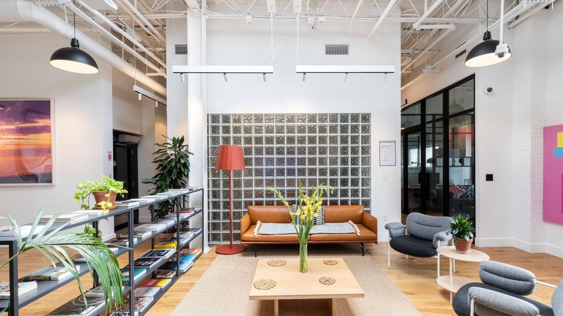 Common Area in the WeWork at College park with couches, modern style reading chairs, and open shelves of books, magazines, and other publications. Green office plants also decorate the space