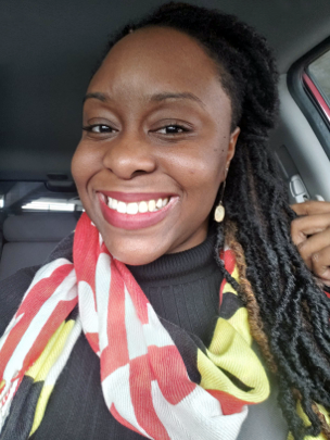 Woman with long hair, a black shirt, and a red, yellow, and black scarf smiling