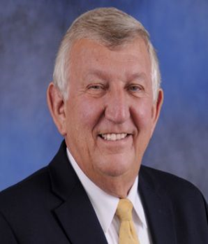 Full color headshot of Senator Ed DeGrange, Sr. smiling with black blazer, white dress shirt, and gold tie against a multicolored background