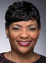 Full color photo of Adrienne Jones smiling wearing a black top against a gray background