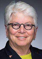 Full color headshot of Maggie McIntosh smiling against a gray background in a black blazer and yellow shirt.