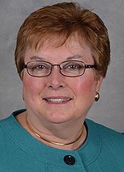 Full color photo of Nancy King wearing a turquoise top and smiling against a gray background.